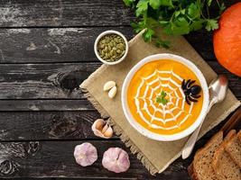 Funny food for Halloween. Pumpkin puree soup, spider web, dark old wooden table, top view, copy space photo
