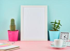 Mockup with blank white frame, alarm, notepad, cup of coffee or tea on pink table photo