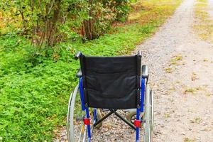 Empty wheelchair standing on road in hospital park waiting for patient services. Invalid chair for disabled people parked outdoor in nature. Handicap accessible symbol. Health care medical concept. photo