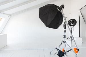 Empty photo studio with lighting equipment. Photographer workplace interior with professional tool set gear. Flash light white background scenes ready for studio shooting. Modern photographer studio