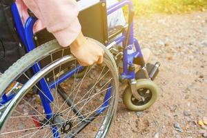 mujer con discapacidad manual en la rueda de la silla de ruedas en la carretera en el parque del hospital esperando los servicios del paciente. niña paralizada irreconocible en silla inválida para personas discapacitadas al aire libre. concepto de rehabilitación. foto