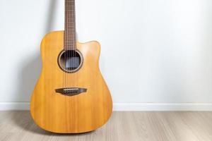 An acoustic dreadnought guitar leaned against the white wall of the room background. photo