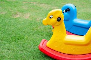 Colorful plastic rocking horse in the backyard. Lay on green grass background. photo