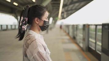 jeune femme asiatique en masque noir debout sur le quai de la station de métro, pandémie de covid19, dame seule à l'intérieur de la nouvelle vie normale de la gare du ciel, faire la queue, transport en commun, lumière du jour