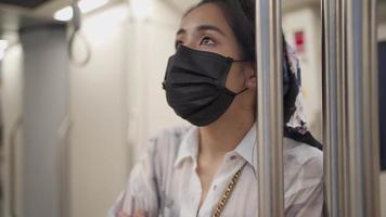 giovane donna asiatica indossa una maschera protettiva nera, guardando l'orario della stazione sul treno della metropolitana, nuovo stile di vita normale distanza sociale, autoprotezione, vagone della metropolitana vuoto, rischio infettivo attenzione al rallentatore video