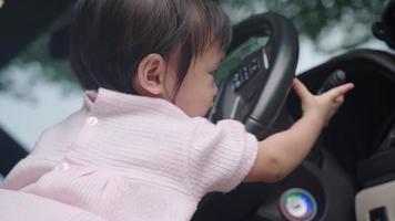 Cute Asian female toddler sitting on car driver front seat playing with steering wheel, childhood memories and curiosity, happy and joyful child learning skills experiences, pure and innocence girl video