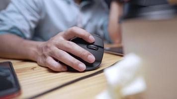 Close up of hand holding black computer mouse on a wooden desk, working equipment with a PC, office working tools, background of people working in modern home office, gamer playing in the video game
