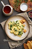 Scrambled eggs with spinach, cup of tea on dark brown background. Vertical photo