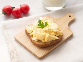 Sandwich with pan-fried scrambled eggs on wooden cutting board, side view. photo