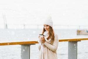 Beautiful young girl drinking coffee, tea from a plastic mug. Winter, Christmas eve, new year's eve. Woman with long hair is going on a vacation trip, Scandinavian style