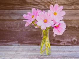jarrón de vidrio con un ramo de flores delicadas y frágiles de color rosa sobre fondo de madera foto
