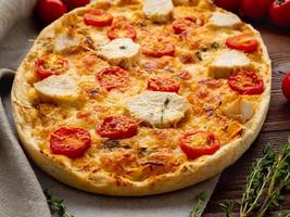 apetitosa focaccia dorada con tomates, carne de pollo, especias en una mesa rústica de madera oscura foto