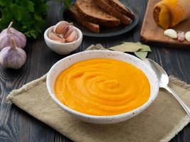 pumpkin soup mashed in a white plate, pumpkin seeds, bread, garlic on dark wooden background photo