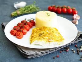 Fish cod baked in oven with mashed potatoes, tomatoes, diet healthy food. Dark gray background photo