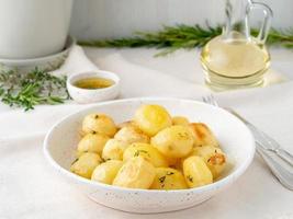 baked in oven with spices round whole potato tubers in plate on white textile background, golden with crust, side view photo