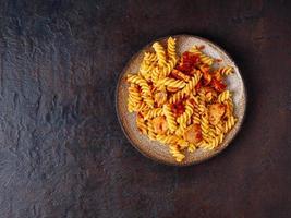 fusilli pasta with tomato sauce, chicken fillet on dark stone concrete background, cope space, top view photo