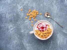 Greek yogurt with jam in white bowl on grey blue concrete stone table, top view, copy space photo