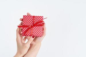 woman hands holding red gift with ribbon, manicured hands with nail polish