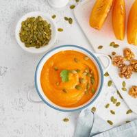Creamy pumpkin soup with seeds, top view light white background