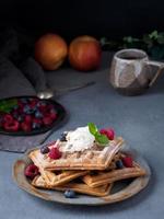 Belgian waffles with raspberries, chocolate syrup. Breakfast with tea on dark background, side view, vertical photo