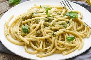 Pesto spaghetti pasta with basil, garlic, pine nuts, olive oil. Rustic table, close up photo