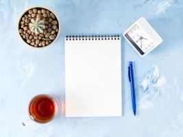 Top view of modern bright blue office desktop with notepad, clock, flower succulent. photo