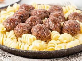 Swedish meatballs with fusilli paste on white wooden table, side view photo