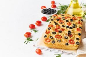 Focaccia with tomatoes, olives and rosemary, copy space, side view. Whole Italian flat bread,