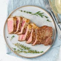 Keto ketogenic diet beef steak, striploin on gray plate on white background. Paleo food