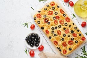 Focaccia with tomatoes, olives and rosemary, copy space, top view. Whole Italian flat bread photo