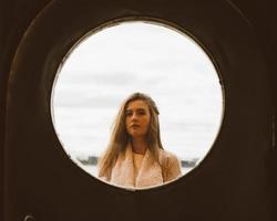 The face of young girl in round frame window on background of sea, ocean, on waterfront. Portrait in circle, backlit photo