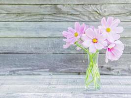 glass vase with a bouquet of pink delicate fragile flowers on wooden background photo