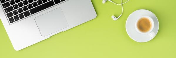 Banner of metallic laptop keyboard, white earphones and coffee cup on light green background photo