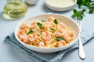 espaguetis de pasta con gambas fritas, salsa bechamel, hoja de menta sobre mesa azul foto