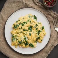 Pan-fried scrambled eggs and spinach, cup of tea on dark brown background. photo