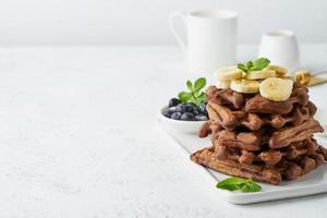 Chocolate banana waffles with maple syrup on white table, copy space, side view. photo