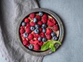 Blueberries and raspberries on plate. A mix of berries on dark background