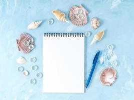 Mock up with frame of seashell and notepad on blue backdrop, scallop shell, copy space.