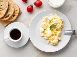 Breakfast with pan-fried scrambled eggs, cup of coffee, tomatoes on white stone background. Omelette, top view