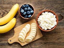 Brown wooden Bowl of homemade curd with banana, jam, blueberries photo