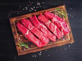 Raw meat, beef steak with seasoning on chopping board on dark background with rosemary, photo