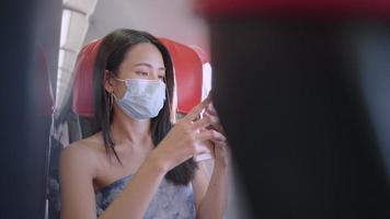 Asian female passenger wear face mask using smart phone onboard airplane, scene inside aircraft cabin, relaxed comfortable new normal travel, public transportation, turn on airplane flight mode video