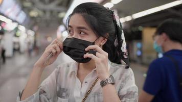 asiatisk kvinna bär svart mask som står och tittar på kameran i sky train station, covid, kvinna inuti tunnelbanestationen, ny normal livsstil, självskydd, kollektivtrafik, kvällsvitt ljus video