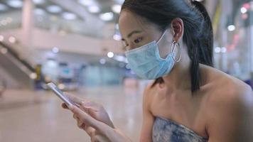 Asian beautiful lady wear face mask using smart phone sit down inside public building, new normal places check-in tracking, relaxed comfortable new normal travel, Corona virus, mobile application user video