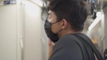 homem asiático usa máscara protetora preta conversando por telefone no metrô, viajante de trem voltando para casa, covid-19 novo normal, autoproteção no transporte público, distanciamento social