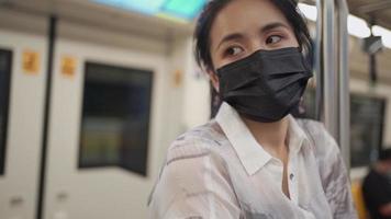 asiatische frau in schwarzer schutzmaske, die in die kamera blickt, am stangenständer in der mitte des zugwagens festhalten, u-bahnstation, covid-19, soziales distanzierungskonzept, neuer normaler lebensstil, zeitlupe