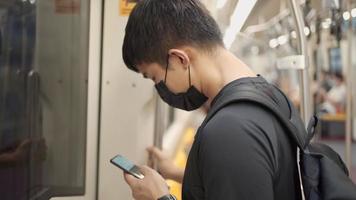 Asian man Wear black mask standing inside sky train head down scrolling phone, Commuter on rail ride, covid-19 new normal, risk on public transport, social distance, smartphone user on the train video