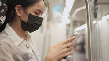 Close up shot Asian young woman in black protective mask stand and use mobile phone in subway train, covid-19 new normal, self protection on public transport, social distancing, new normal lifestyle video