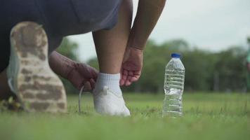 shot from behind man tying shoes laces on green grass field during Exercise at the park Background, outdoor exercising, active lifestyle, stay hydrate, mineral water bottle on the side, rear view