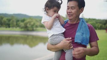 A generational diversity family concept, An active strong grandfather holding his cute granddaughter while standing in public park on weekend, family member gathering together, happy retirement life video